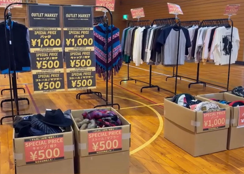 
										    体育館に置かれた複数のハンガーラックにたくさんの洋服がかけられて、
										    床に置かれたダンボールには帽子やマフラーなどの様々なファッション小物が入っています
										  