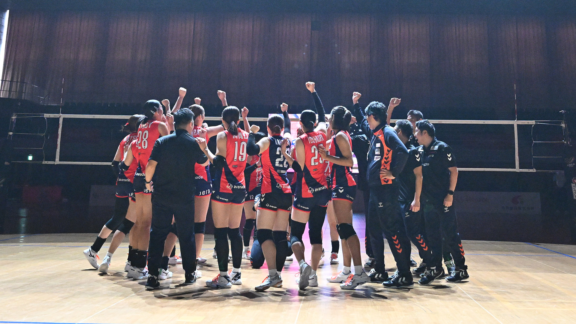 
					    スポットライトの当たるバレーボールコートの中央で円陣を組み、右手を掲げるアランマーレ山形の選手とスタッフの様子です
					  